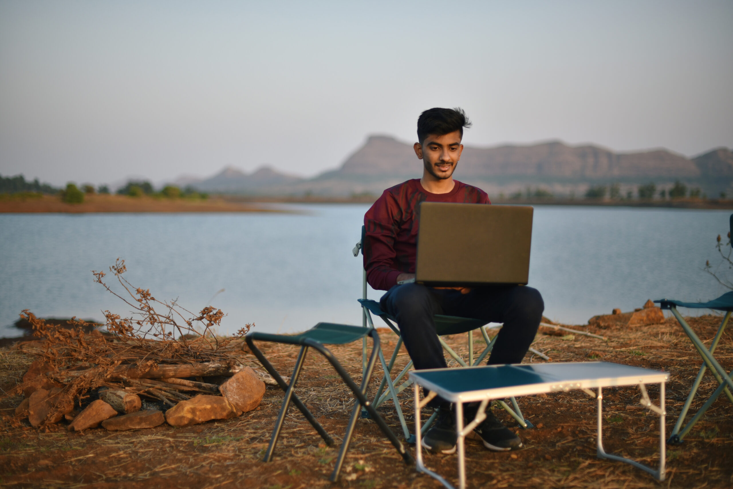 Young man working on laptop while enjoying the serenity at Vaitarna dam, Maharashtra in India